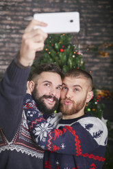 Porträt eines glücklichen schwulen Paares, das zu Weihnachten zu Hause ein Selfie mit dem Smartphone macht - RTBF01052