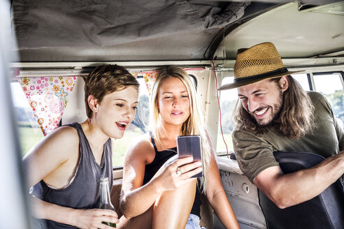 Glückliche Freunde im Lieferwagen mit Blick auf das Smartphone - FMKF04538