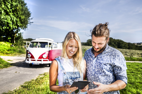 Happy couple outside van in rural landscape looking at tablet stock photo