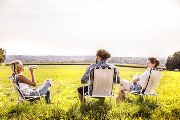 Freunde sitzen auf Campingstühlen in ländlicher Landschaft - FMKF04550