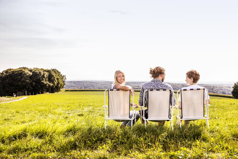 Freunde sitzen auf Campingstühlen in ländlicher Landschaft - FMKF04551