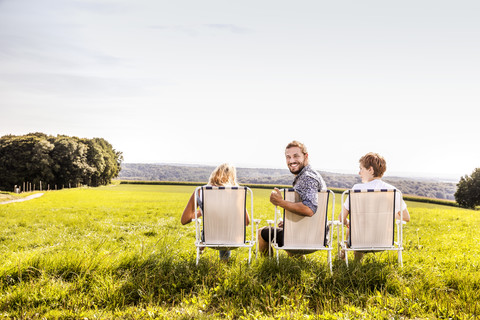 Friends sitting on camping chairs in rural landscape stock photo