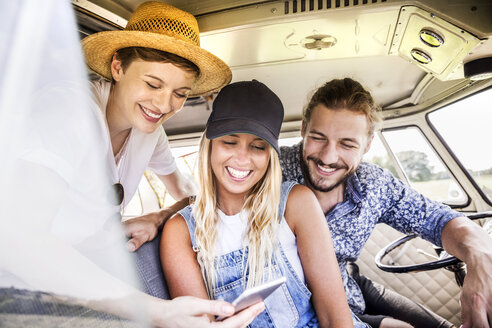 Glückliche Freunde im Lieferwagen mit Blick auf das Smartphone - FMKF04562