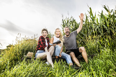 Carefree friends with tablet sitting at a cornfield - FMKF04574