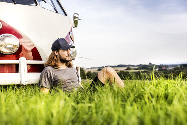 Junger Mann sitzt an einem Lieferwagen auf einem Feld in ländlicher Landschaft - FMKF04576