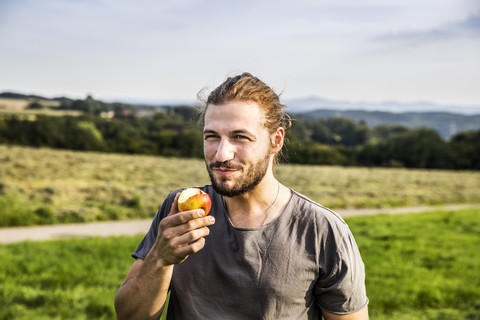Junger Mann isst einen Apfel in ländlicher Landschaft, lizenzfreies Stockfoto