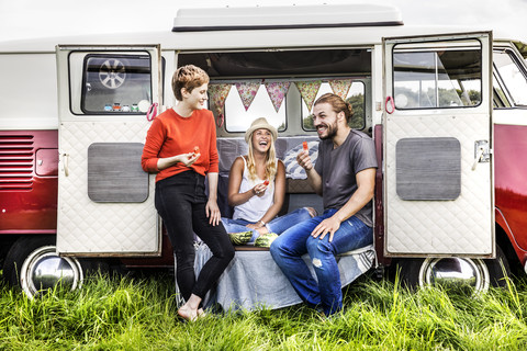 Glückliche Freunde beim Picknick in einem auf einem Feld geparkten Lieferwagen, lizenzfreies Stockfoto
