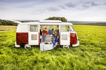 Friends having picnic in a van parked on field in rural landscape - FMKF04584