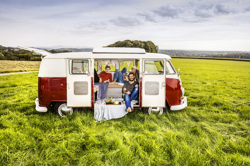 Freunde machen ein Picknick in einem auf einem Feld geparkten Lieferwagen in einer ländlichen Landschaft - FMKF04584