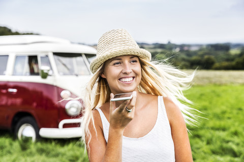 Happy young woman with cell phone in front of van in rural landscape stock photo