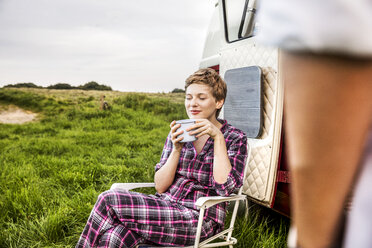 Frau im Pyjama genießt Kaffee an einem Lieferwagen in ländlicher Landschaft - FMKF04595