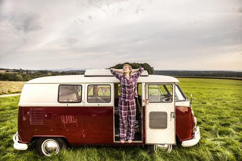 Woman in pyjama stretching in a van in rural landscape stock photo
