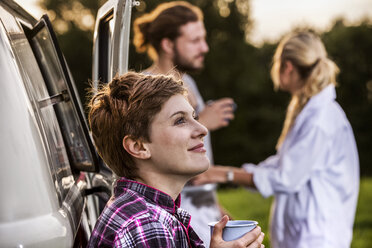 Frau mit Freunden genießt Kaffee an einem Lieferwagen in ländlicher Landschaft - FMKF04610