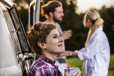 Woman with friends enjoying coffee at a van in rural landscape - FMKF04610