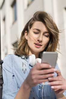Porträt einer Frau mit Kopfhörern, die auf ihr Mobiltelefon schaut - PNEF00164