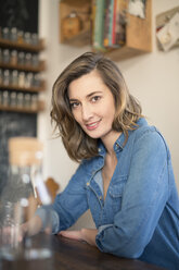 Portrait of smiling woman leaning on kitchen table - PNEF00167