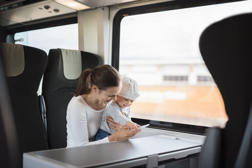 Mutter mit kleinem Mädchen reist mit dem Zug und schaut auf ihr Handy - DIGF02872