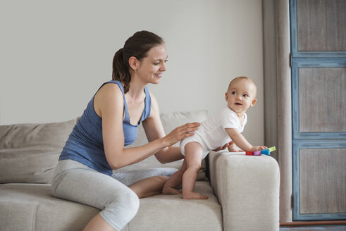 Glückliches kleines Mädchen mit Mutter, die auf der Couch spielt - DIGF02889