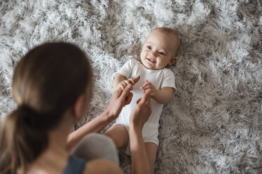 Baby girl lying on carpet at home looking at mother - DIGF02890