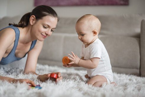 Happy baby girl with mother playing on carpet at home - DIGF02891