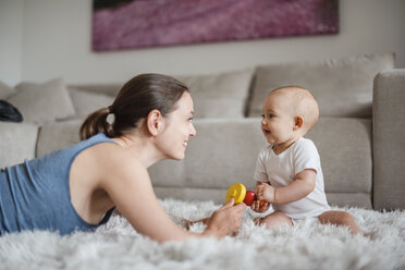 Glückliches kleines Mädchen mit Mutter, die zu Hause auf dem Teppich spielt - DIGF02892