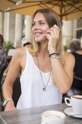 Junge Frau in einem Straßencafé, die mit ihrem Handy telefoniert und sich umschaut - JUNF00918