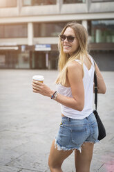 Smiling young woman holding takeaway coffee in the city - JUNF00922