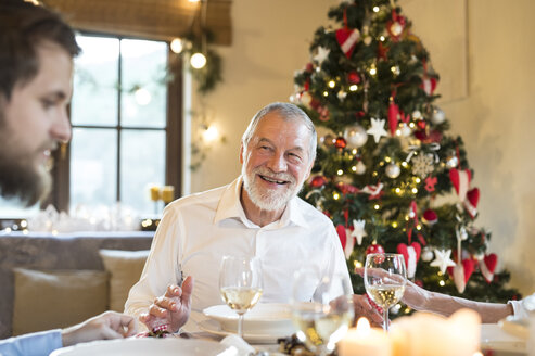 Lächelnder älterer Mann, der seinen erwachsenen Sohn beim Weihnachtsessen ansieht - HAPF02193