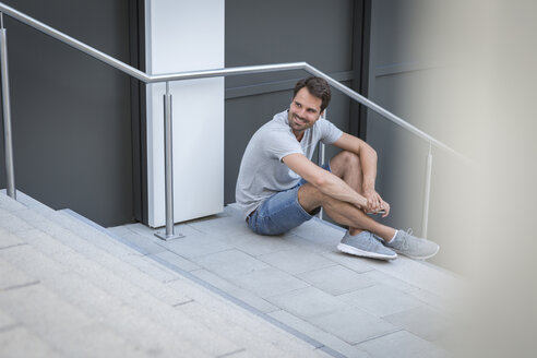 Mann sitzt auf einer Treppe und lächelt - JUNF00941