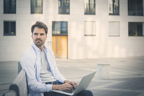 Mann in der Stadt, der auf einer Bank sitzt und einen Laptop benutzt, lizenzfreies Stockfoto