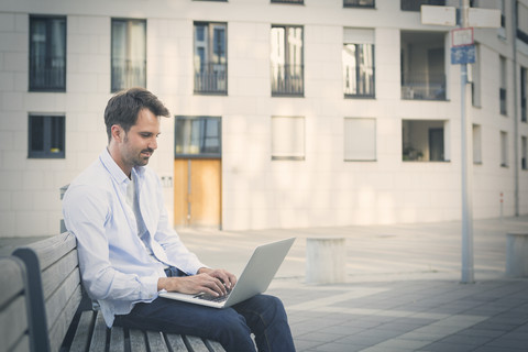 Mann in der Stadt, der auf einer Bank sitzt und einen Laptop benutzt, lizenzfreies Stockfoto