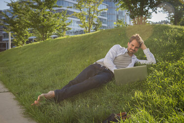 Man lying on grass using his laptop - JUNF00945