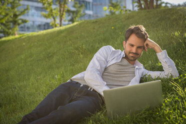 Mann liegt im Gras und benutzt seinen Laptop - JUNF00946