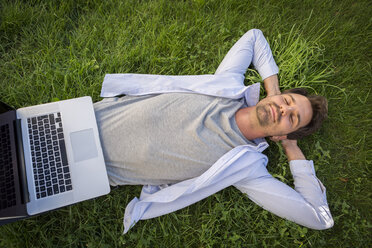 Mann, der sich im Sommer im Gras entspannt, mit Laptop auf dem Bauch - JUNF00948