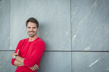 Smiling man leaning against wall with arms crossed - JUNF00959