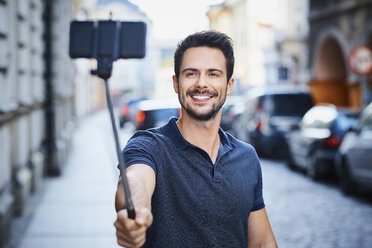 Man taking photo with smartphone mounted on selfie stick - BSZF00073