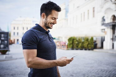 Smiling man using cell phone in the city - BSZF00075