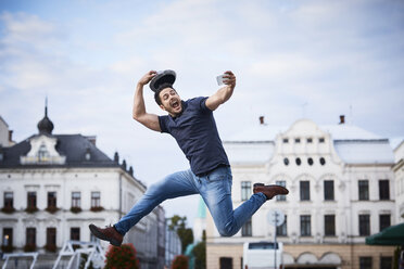 Man jumping and taking selfie holding fedora hat - BSZF00079