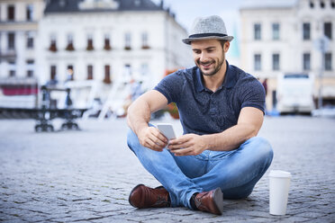 Man sitting on city square using phone - BSZF00081