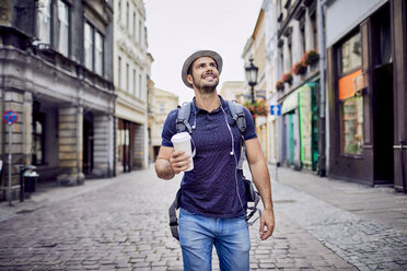 Traveler with backpack walking down city street and holding coffe - BSZF00084