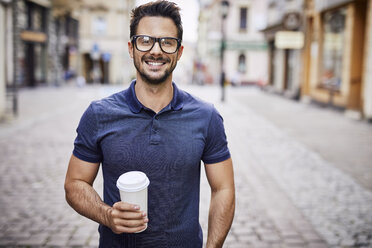 Porträt eines lächelnden Mannes mit Brille, der einen Kaffee im Freien hält - BSZF00086