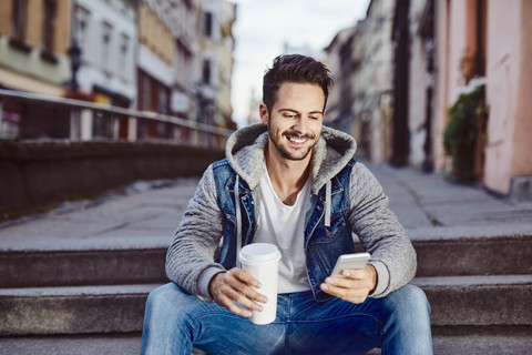 Man with coffee sitting on stairs in the city using phone stock photo