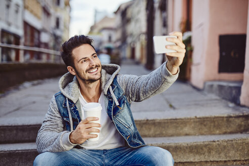 Mann macht Selfie mit Kaffee und sitzt auf einer Treppe - BSZF00092