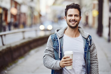 Porträt eines lächelnden Mannes mit Kaffee in der Hand und Stadtstraße im Hintergrund - BSZF00094