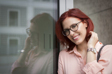 Young businesswoman leaning against glass pane, smiling - JUNF00992