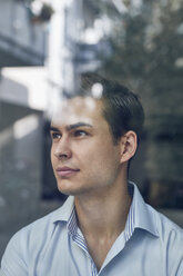 Portrait of young businessman behind glass pane in office - PNEF00172