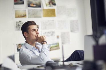 Portrait of pensive young businessman sitting at desk in the office - PNEF00175