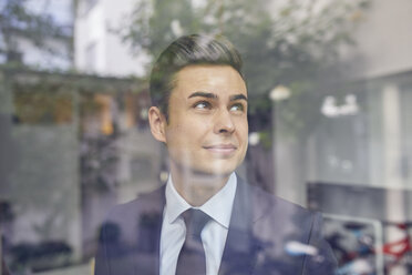 Porträt eines jungen Geschäftsmannes hinter einer Glasscheibe in einem Büro mit Blick nach oben - PNEF00178