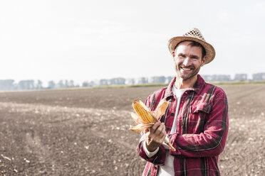 Portrait of smiling farmer on field holding corn cob - UUF11909