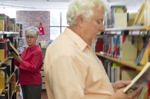 Senior woman watching man reading book in a city library stock photo